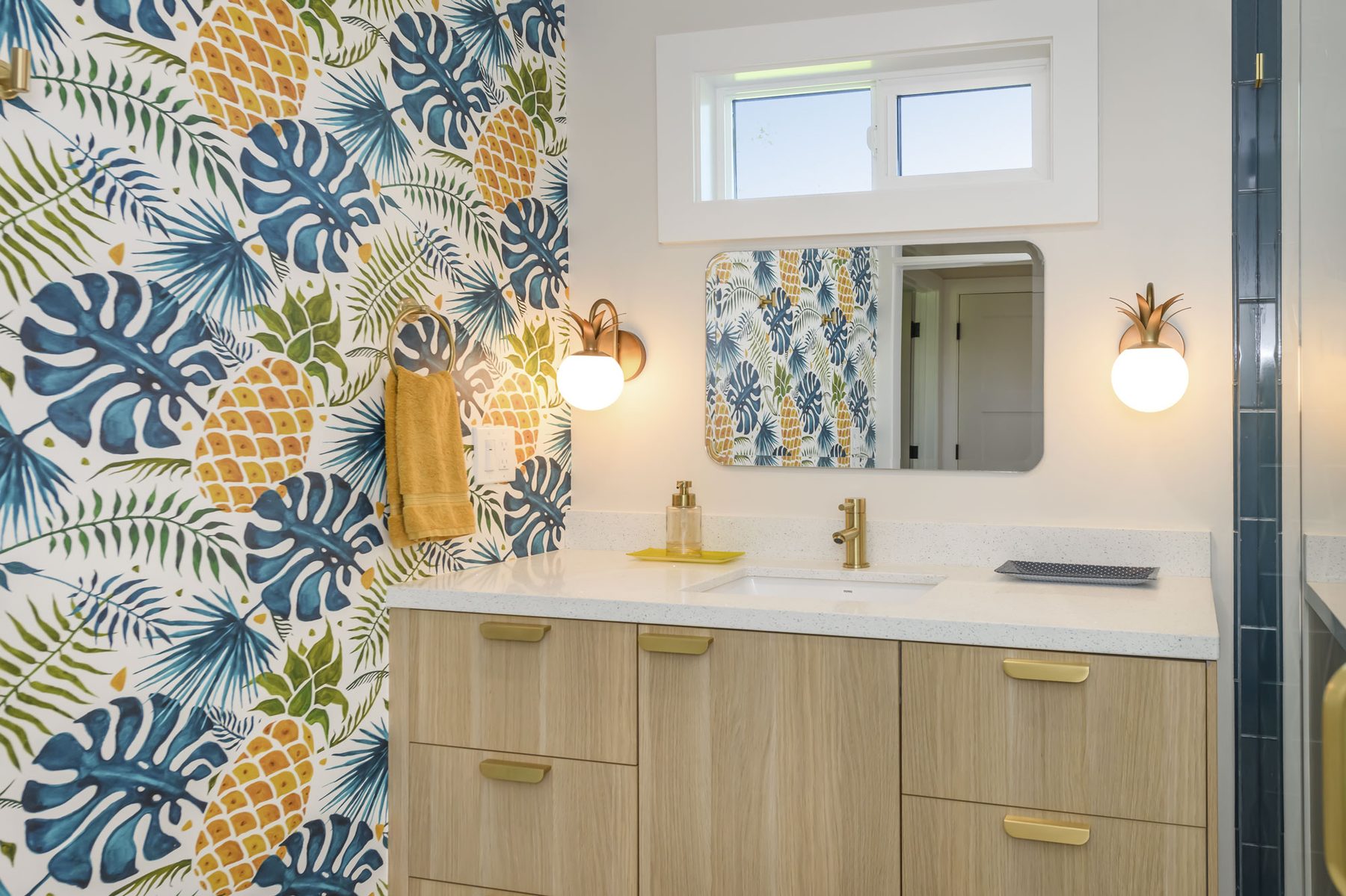 Tiki-themed guest bath with monstera and pineapple wallpaper and brass sconces