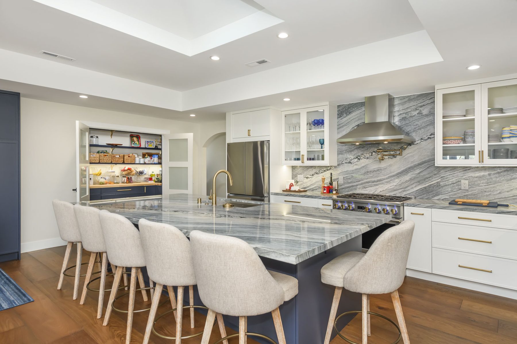 Wide view of kitchen island with quartzite counter and upholstered counter-height seating for seven