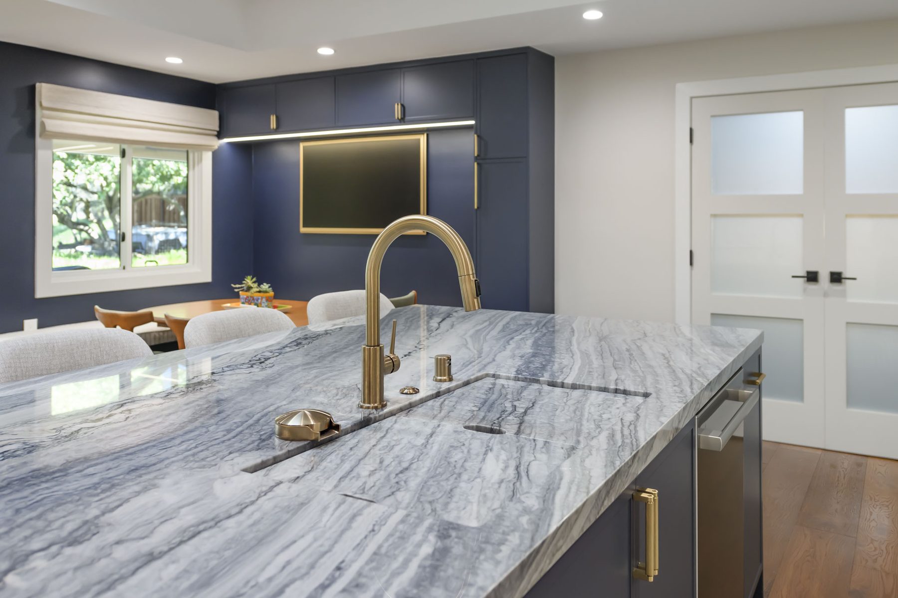 Island sink detail with brass faucet, garbage disposal air switch, and view through to breakfast nook
