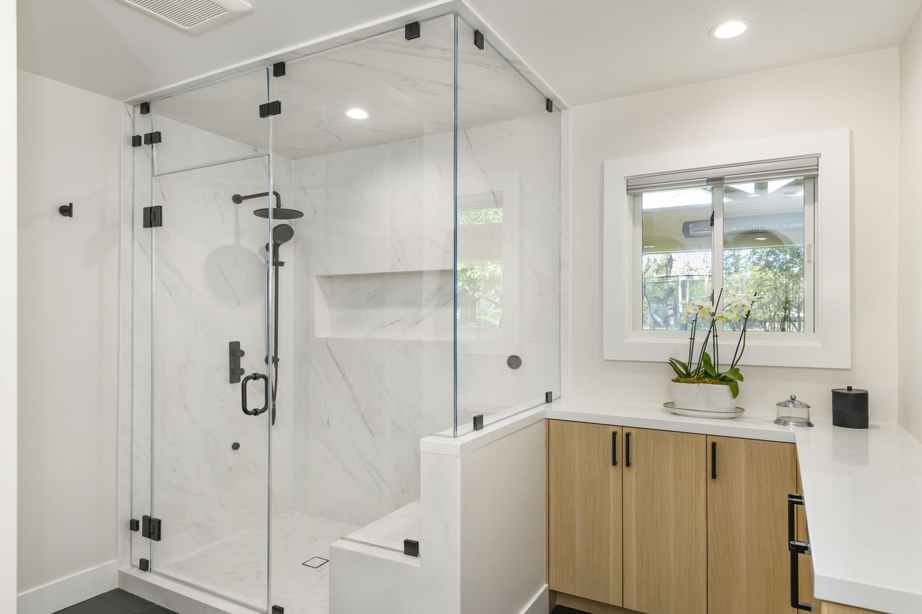 Primary suite shower in large-format white marble porcelain with matte black fixtures