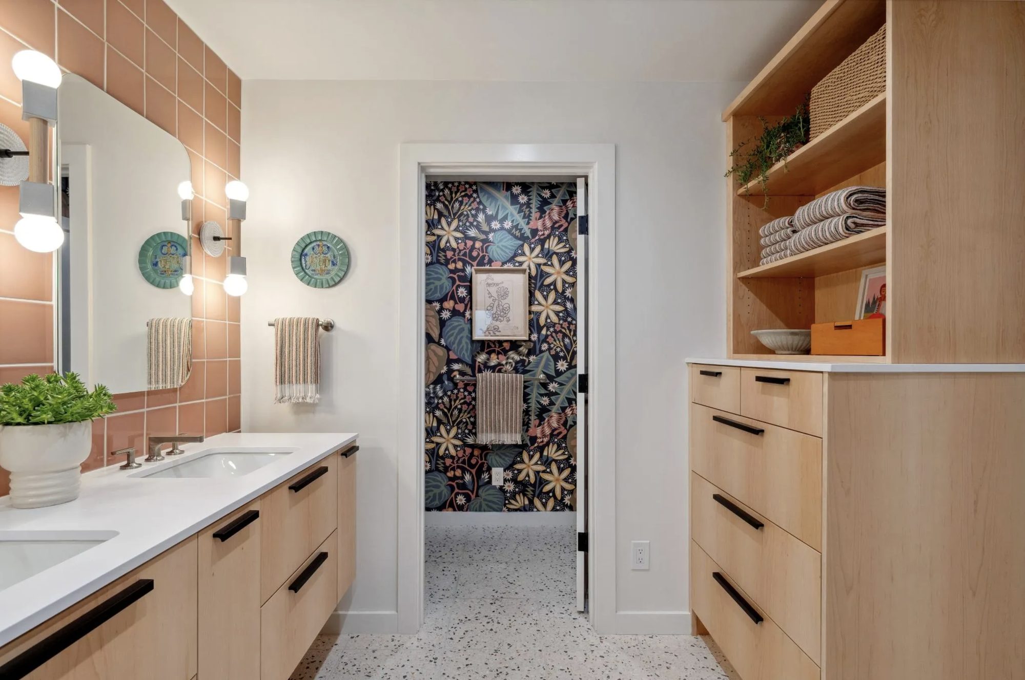 Primary bath in peach tile and light oak opening to a botanical powder room