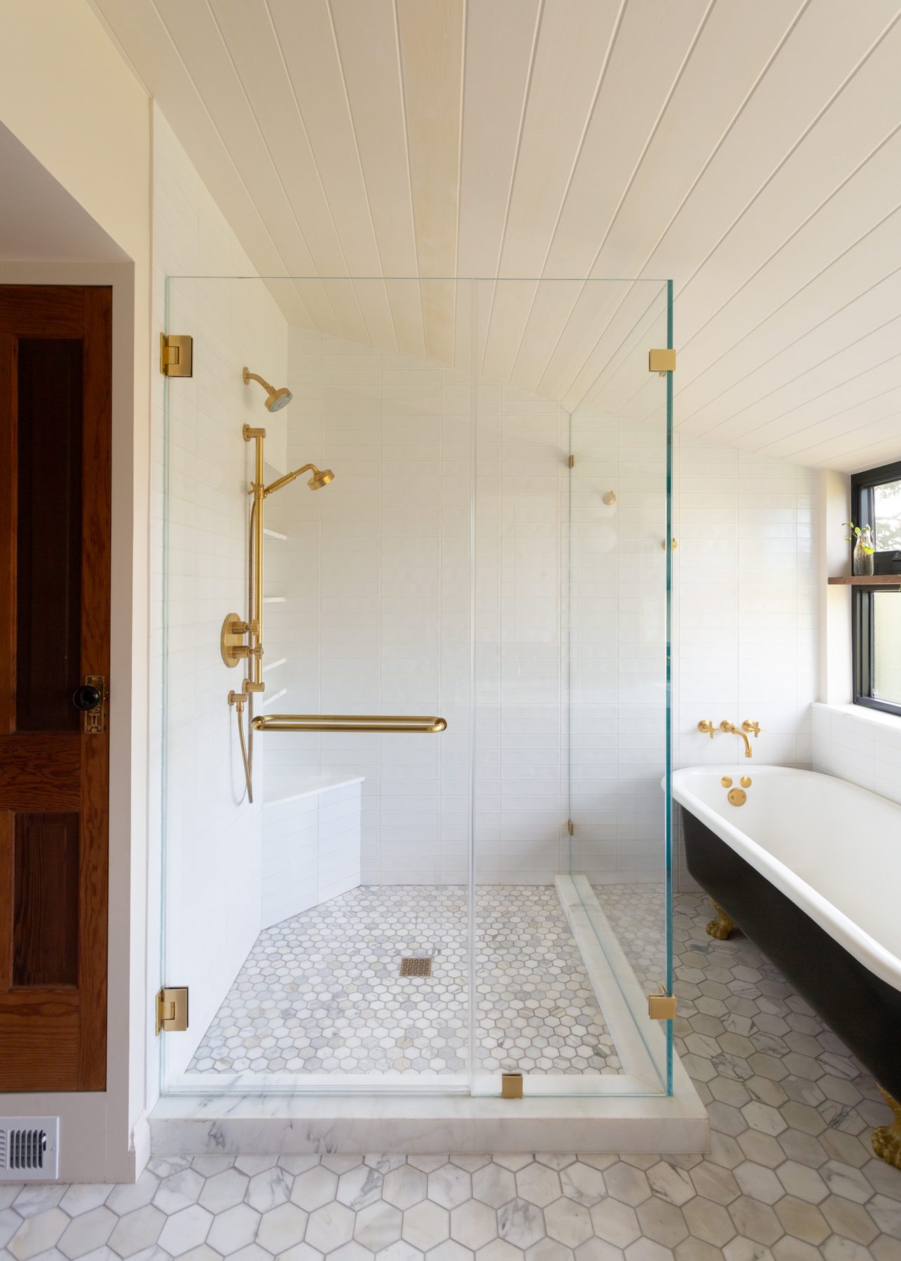 Brass-fitted glass shower beside a black clawfoot soaking tub