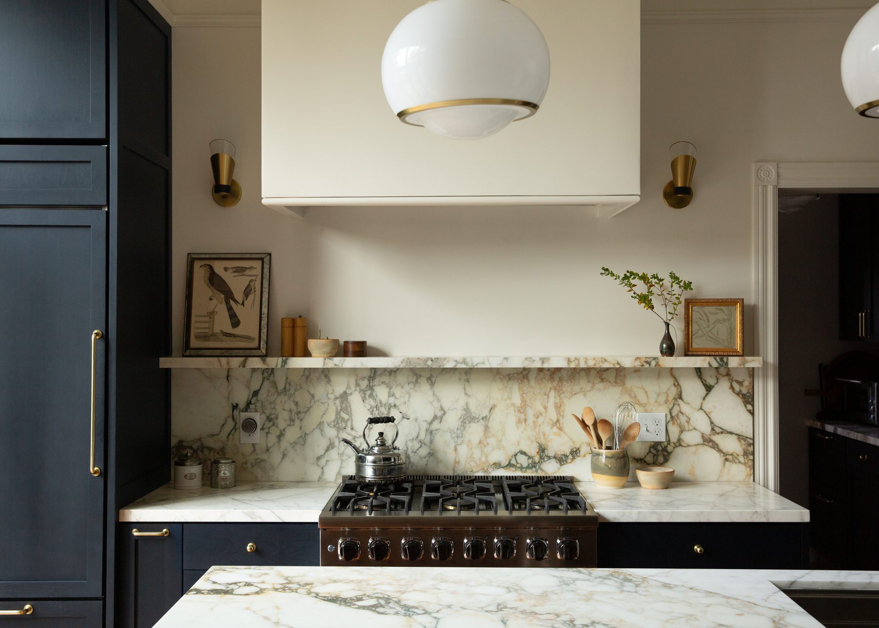Range detail with marble backsplash, open shelf, and brass sconces